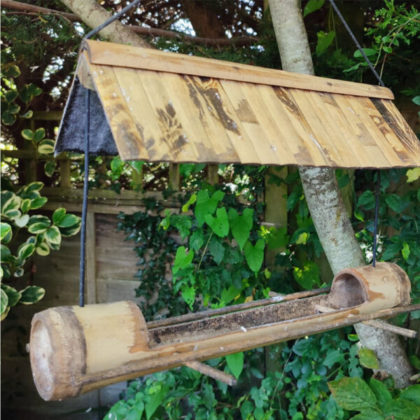 A bamboo bird feeder hangs from a tree in a customer's garden