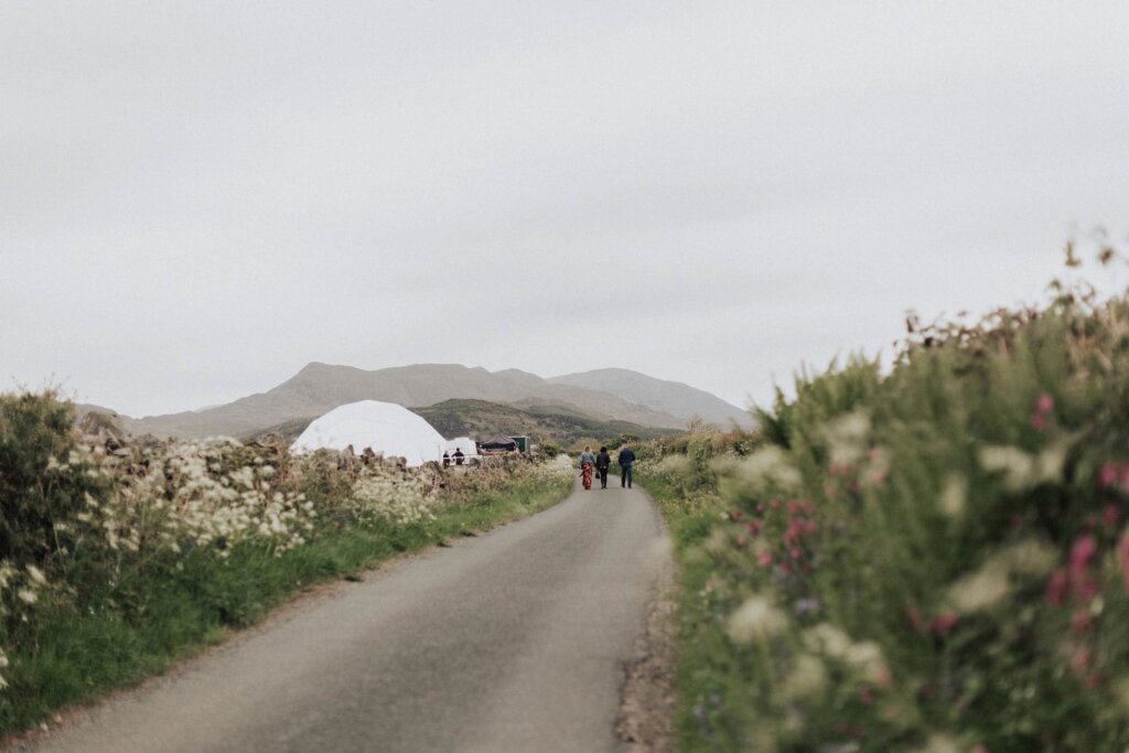 People walking up the road toward a bamboo geodesic dome in the distance by Atlas Domes